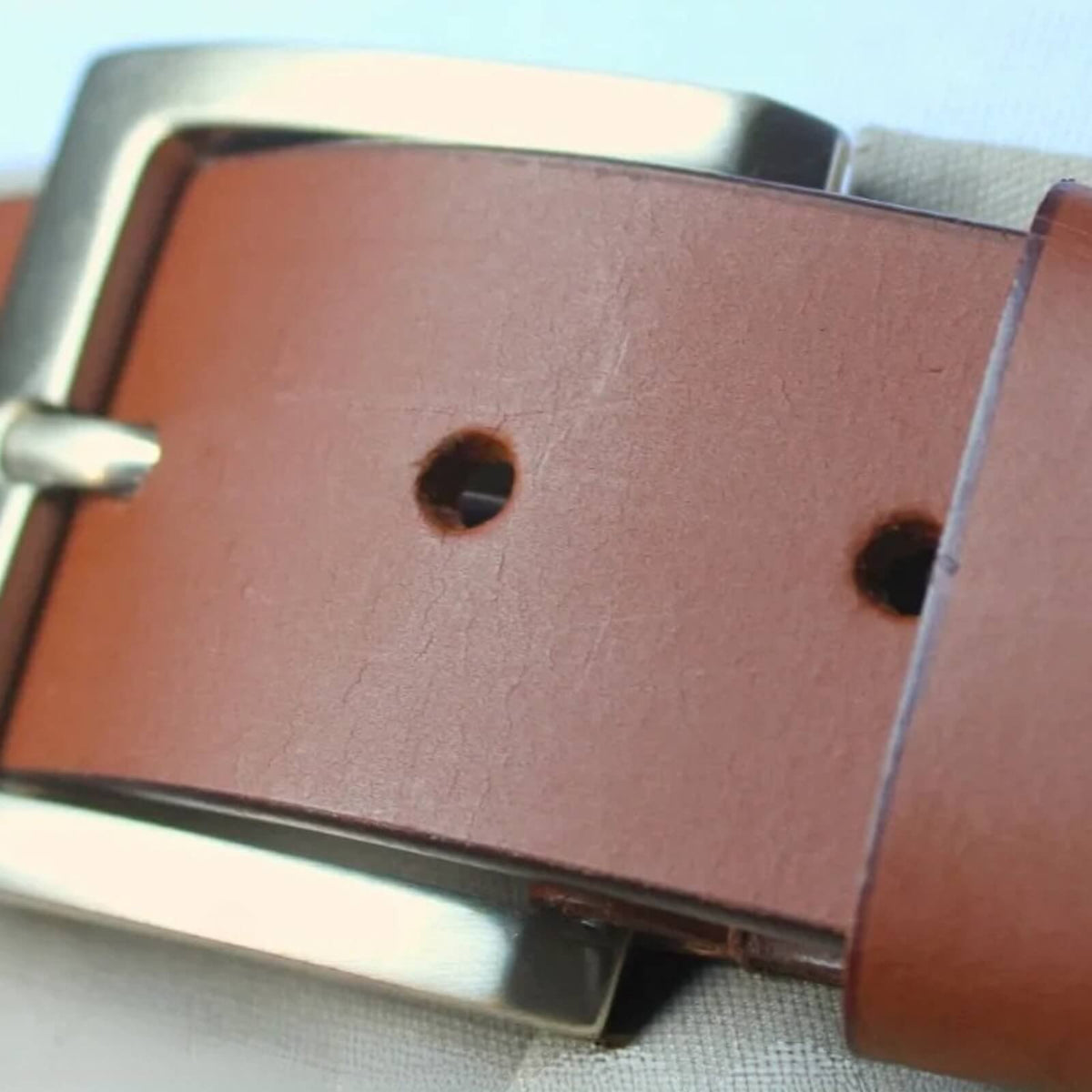 Brown leather belt with silver buckle on a light background