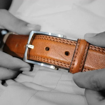 Brown leather belt with silver buckle held by gloved hands against a gray background